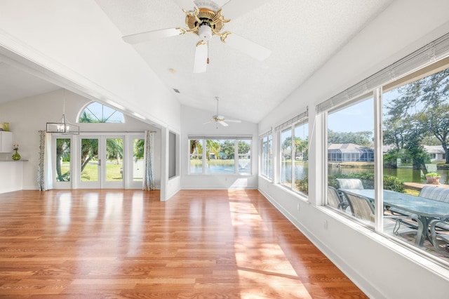 unfurnished sunroom with lofted ceiling, a water view, and ceiling fan with notable chandelier