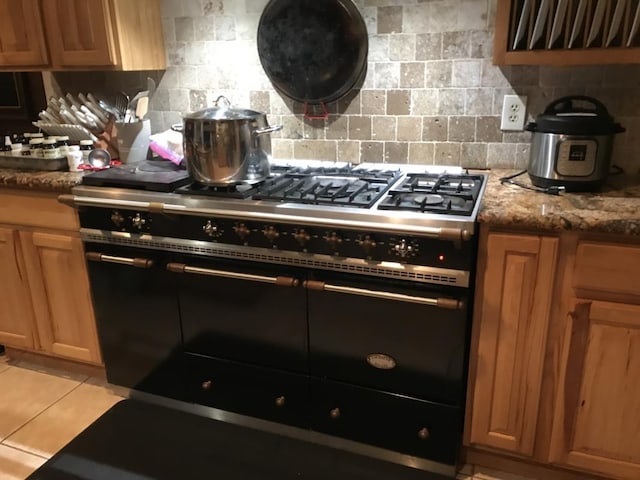 kitchen with light tile patterned floors, backsplash, stone countertops, and high end black range