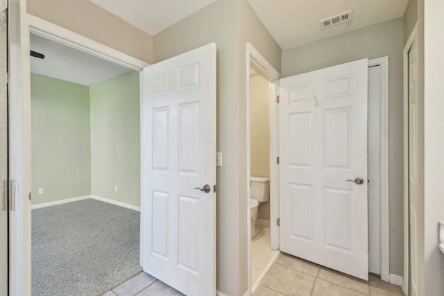 corridor with light tile patterned floors, visible vents, and a textured ceiling