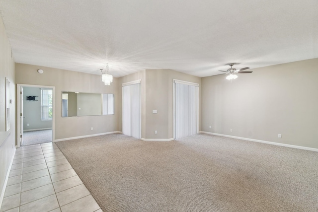 spare room with light carpet, ceiling fan with notable chandelier, baseboards, and light tile patterned flooring