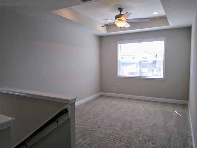 spare room featuring a tray ceiling, light colored carpet, and ceiling fan