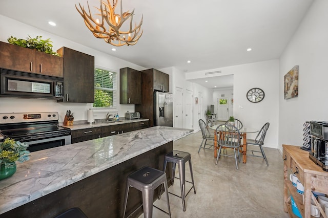 kitchen with dark brown cabinetry, stainless steel appliances, a kitchen bar, and hanging light fixtures