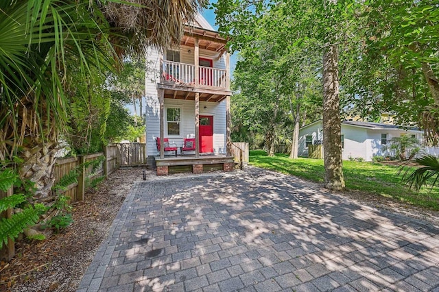 view of front of home featuring a porch, a balcony, fence, and a front lawn