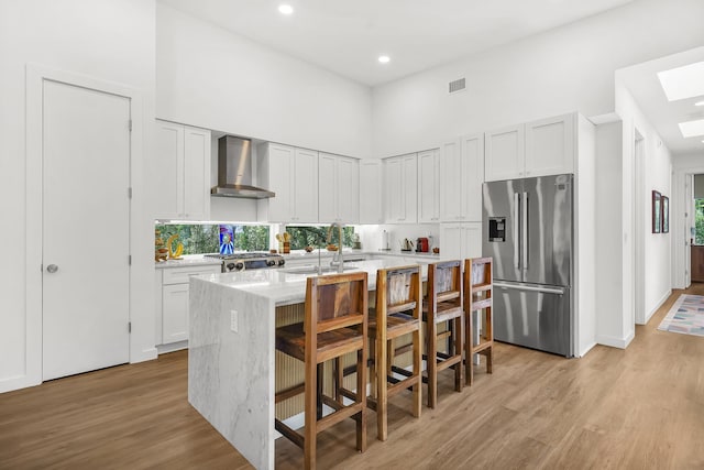 2470 Oleander St, Saint Augustine, FL 32080 - kitchen featuring stainless steel fridge, wall chimney range hood, light wood-style floors, an island with sink, and a breakfast bar area