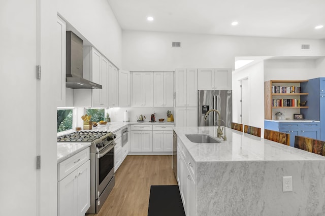 2470 Oleander St, Saint Augustine, FL 32080 - kitchen featuring appliances with stainless steel finishes, wall chimney exhaust hood, an island with sink, white cabinetry, and light wood-style floors