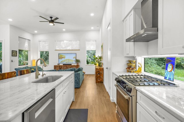 2470 Oleander St, Saint Augustine, FL 32080 - kitchen featuring wall chimney exhaust hood, appliances with stainless steel finishes, light wood finished floors, a ceiling fan, and white cabinetry