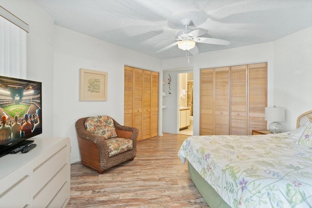 bedroom featuring two closets, ensuite bathroom, light hardwood / wood-style flooring, ceiling fan, and a textured ceiling