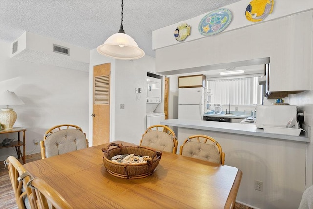 dining room featuring stacked washer / dryer, a textured ceiling, and hardwood / wood-style flooring