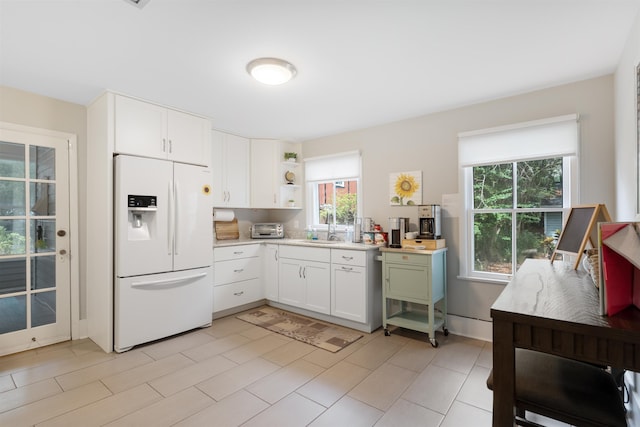 kitchen featuring white refrigerator with ice dispenser, white cabinetry, and sink