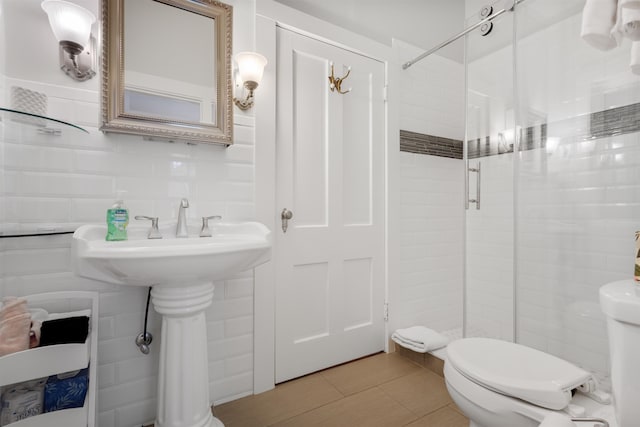 bathroom with tile patterned flooring, backsplash, toilet, a shower with shower door, and tile walls