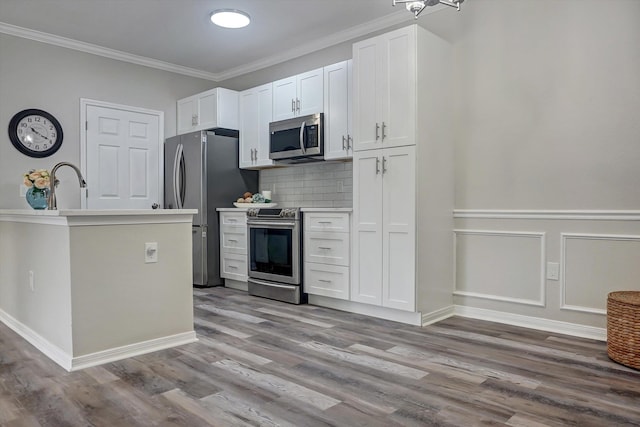 kitchen featuring appliances with stainless steel finishes, backsplash, ornamental molding, light hardwood / wood-style floors, and white cabinetry