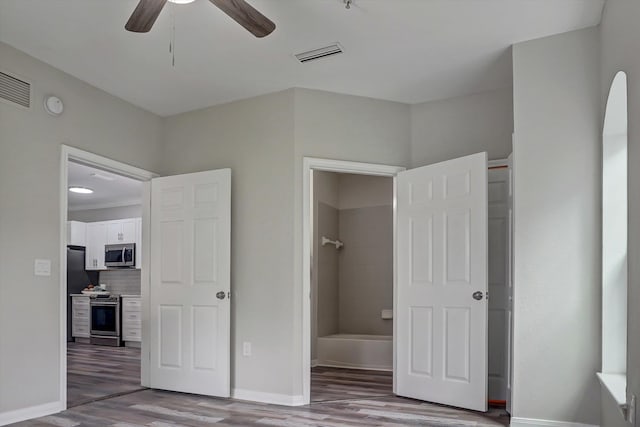 unfurnished bedroom featuring stainless steel refrigerator, ensuite bath, ceiling fan, and light hardwood / wood-style flooring