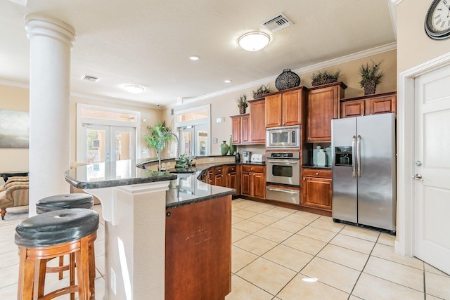 kitchen featuring french doors, a kitchen breakfast bar, decorative columns, appliances with stainless steel finishes, and ornamental molding