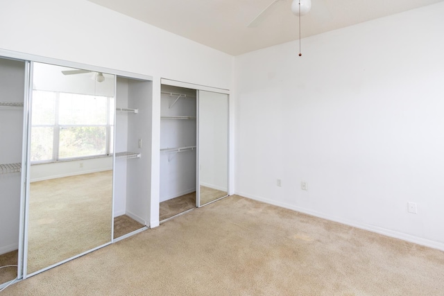 unfurnished bedroom featuring ceiling fan, light colored carpet, and multiple closets