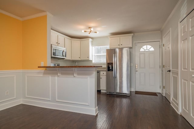 kitchen featuring appliances with stainless steel finishes, white cabinets, a kitchen bar, dark hardwood / wood-style floors, and ornamental molding