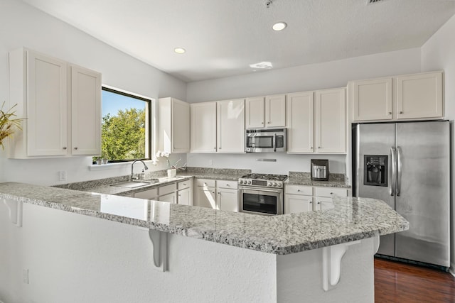 kitchen with white cabinets, appliances with stainless steel finishes, kitchen peninsula, and a kitchen breakfast bar