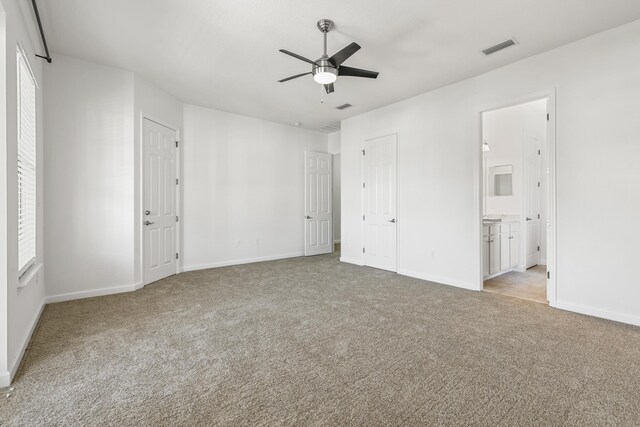 unfurnished bedroom with ensuite bathroom, ceiling fan, light carpet, and multiple windows