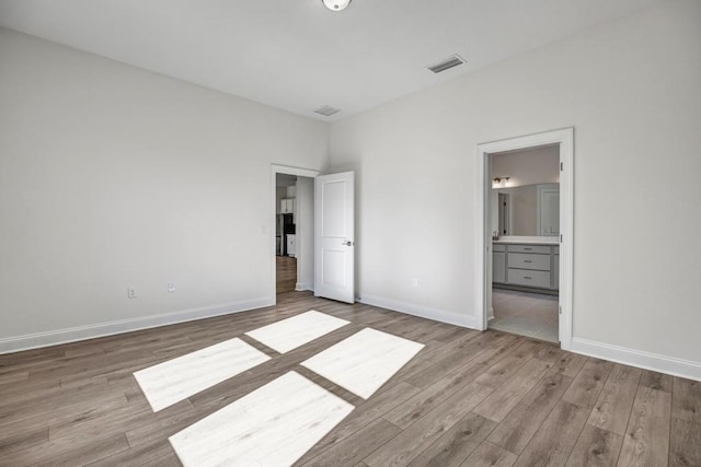 unfurnished bedroom featuring wood finished floors, visible vents, ensuite bath, and baseboards