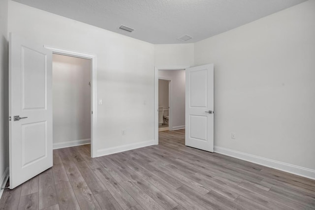 unfurnished bedroom featuring a textured ceiling, visible vents, light wood-style flooring, and baseboards