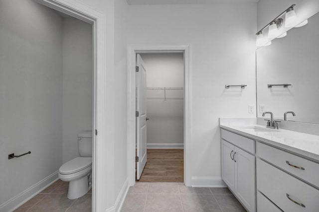 full bath with vanity, toilet, a walk in closet, baseboards, and tile patterned flooring