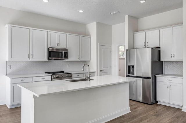 kitchen featuring a kitchen island with sink, a sink, decorative backsplash, appliances with stainless steel finishes, and wood finished floors