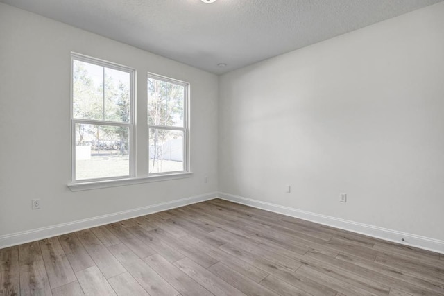 unfurnished room with a textured ceiling, baseboards, and light wood-type flooring