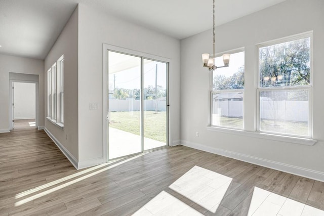 unfurnished dining area featuring wood finished floors, a notable chandelier, and baseboards