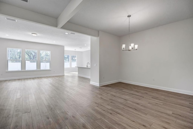 empty room with wood finished floors, a notable chandelier, beamed ceiling, and baseboards