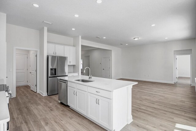 kitchen with recessed lighting, stainless steel appliances, white cabinets, light wood finished floors, and a sink