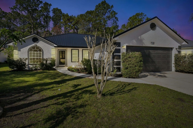 ranch-style house with a garage, concrete driveway, metal roof, a yard, and stucco siding