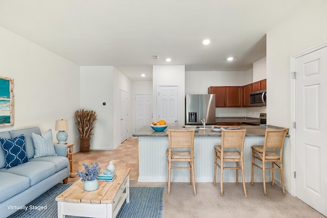 kitchen featuring a kitchen bar, kitchen peninsula, stainless steel appliances, light colored carpet, and sink