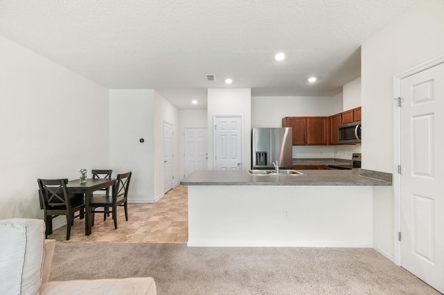 kitchen with light carpet, sink, a textured ceiling, kitchen peninsula, and stainless steel appliances