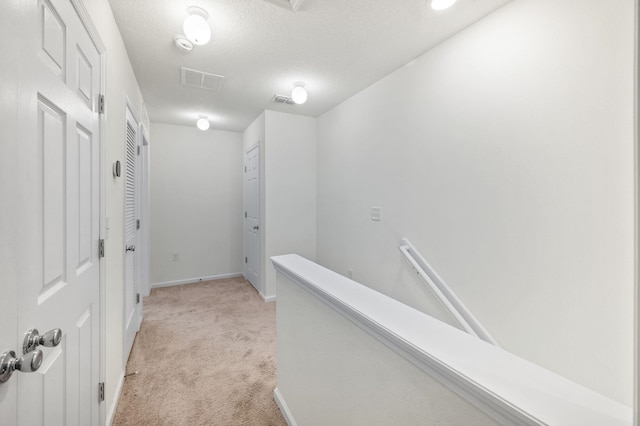 hall with light colored carpet and a textured ceiling