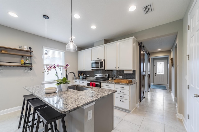 kitchen with sink, hanging light fixtures, stainless steel appliances, light stone counters, and white cabinets