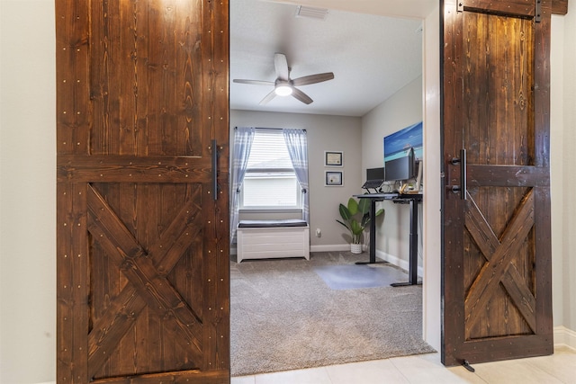 interior space featuring ceiling fan, a barn door, and light carpet