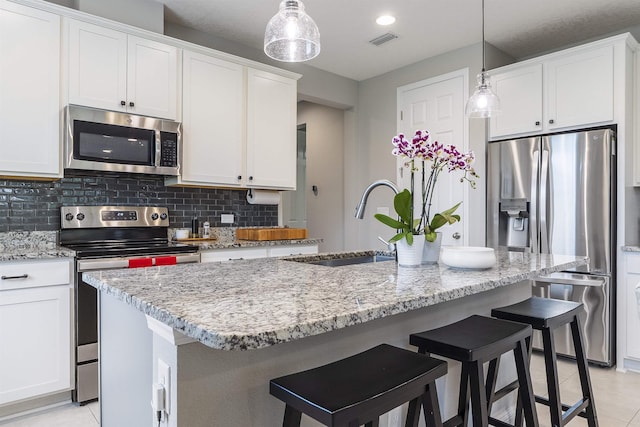 kitchen with pendant lighting, white cabinets, stainless steel appliances, and an island with sink