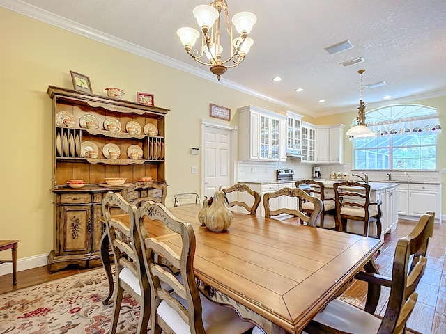 dining area with sink, light hardwood / wood-style floors, a chandelier, a textured ceiling, and ornamental molding