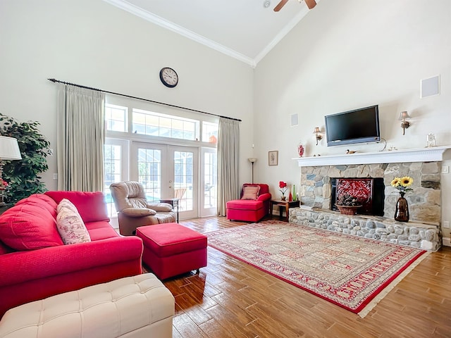 living room with ornamental molding, ceiling fan, wood-type flooring, high vaulted ceiling, and a stone fireplace