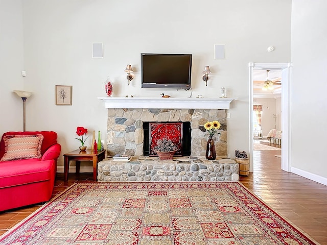 living area featuring a stone fireplace, ceiling fan, and hardwood / wood-style flooring