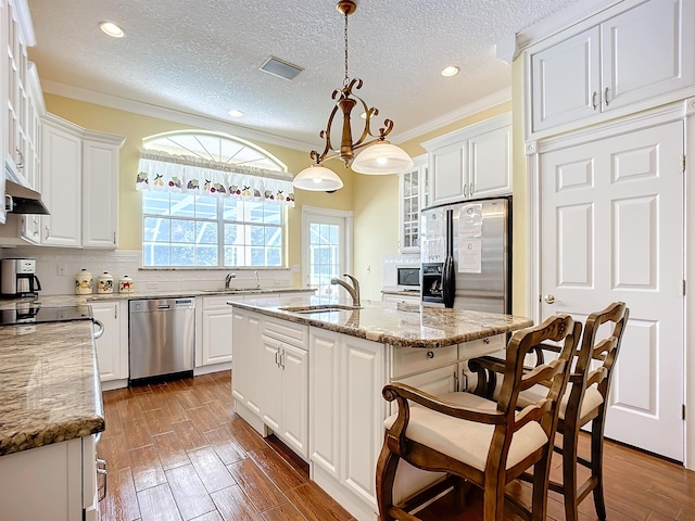 kitchen featuring ornamental molding, white cabinetry, stainless steel appliances, and an island with sink