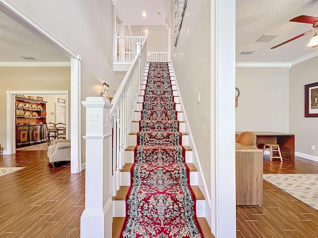 staircase featuring hardwood / wood-style flooring, ceiling fan, ornamental molding, and a textured ceiling