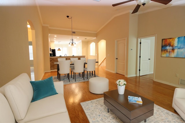 living room featuring vaulted ceiling, wood-type flooring, ceiling fan with notable chandelier, and ornamental molding