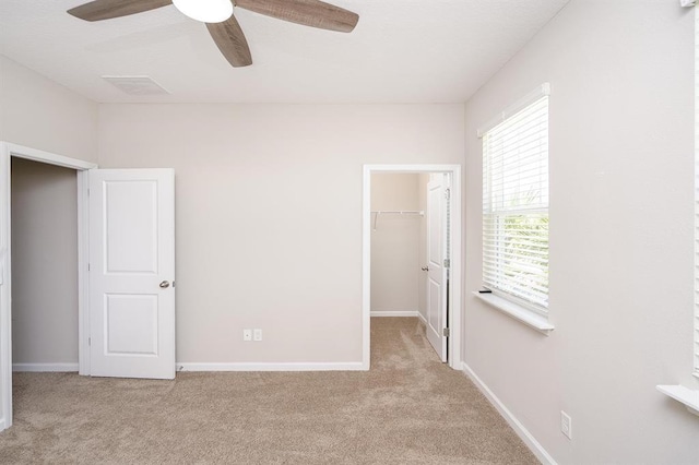 unfurnished bedroom featuring a spacious closet, light colored carpet, ceiling fan, and a closet