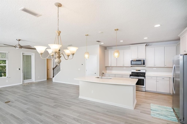 kitchen with a textured ceiling, appliances with stainless steel finishes, pendant lighting, a kitchen island with sink, and white cabinets