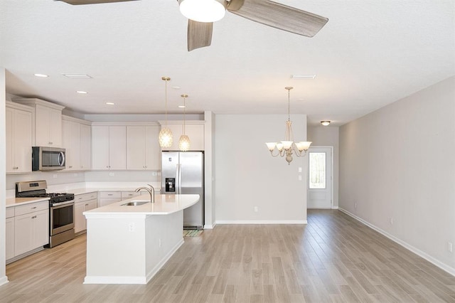 kitchen featuring a kitchen island with sink, sink, stainless steel appliances, and hanging light fixtures