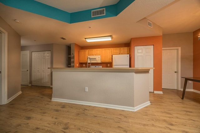 kitchen with an island with sink, light brown cabinets, white appliances, and light hardwood / wood-style flooring