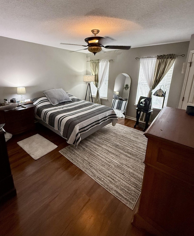 bedroom featuring ceiling fan, dark hardwood / wood-style floors, a textured ceiling, and multiple windows