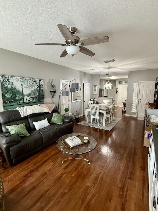 living room with ceiling fan with notable chandelier, a textured ceiling, and dark hardwood / wood-style flooring