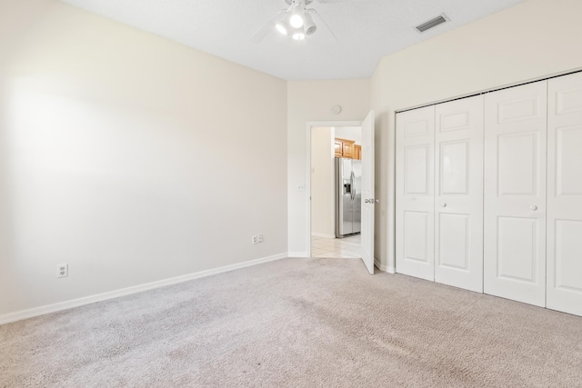 unfurnished bedroom featuring ceiling fan, light carpet, stainless steel fridge with ice dispenser, and a closet