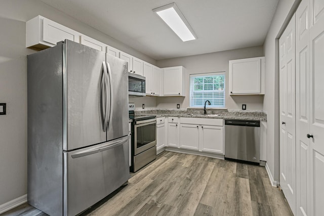 kitchen featuring sink, white cabinetry, light hardwood / wood-style flooring, stainless steel appliances, and light stone countertops